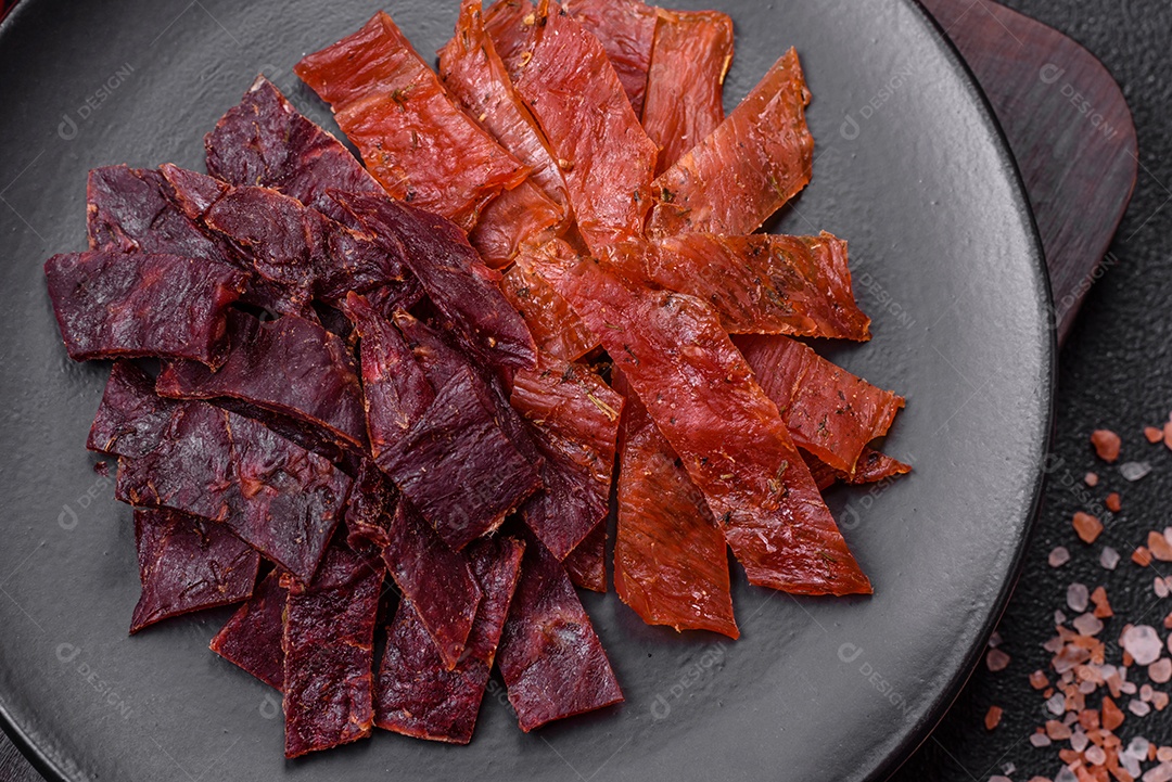 Deliciosa vitela seca ou carne seca de peru com sal, especiarias e ervas sobre um fundo escuro de concreto