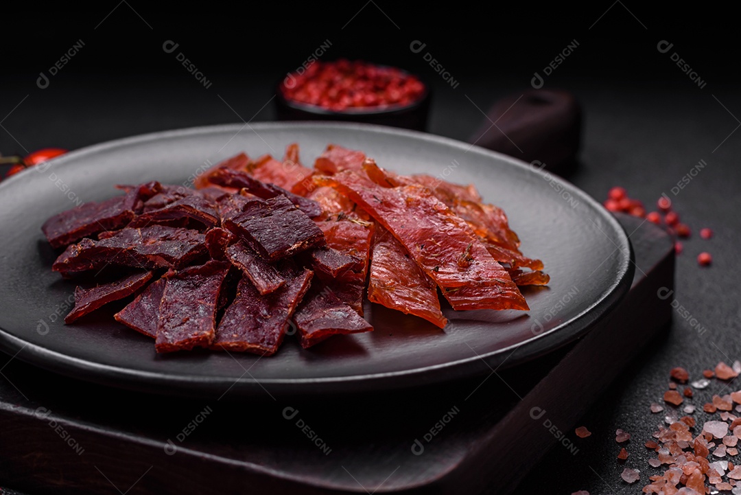 Deliciosa vitela seca ou carne seca de peru com sal, especiarias e ervas sobre um fundo escuro de concreto