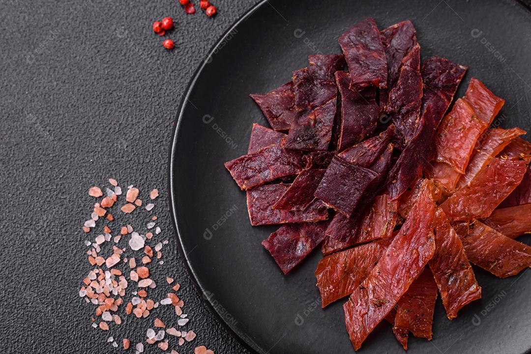 Deliciosa vitela seca ou carne seca de peru com sal, especiarias e ervas sobre um fundo escuro de concreto