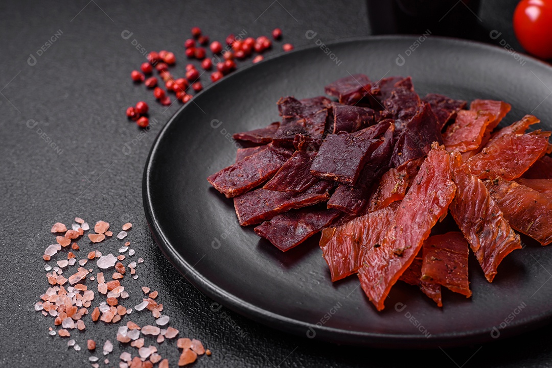 Deliciosa vitela seca ou carne seca de peru com sal, especiarias e ervas sobre um fundo escuro de concreto