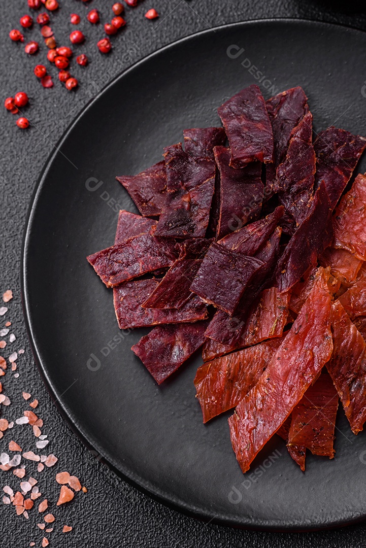 Deliciosa vitela seca ou carne seca de peru com sal, especiarias e ervas sobre um fundo escuro de concreto