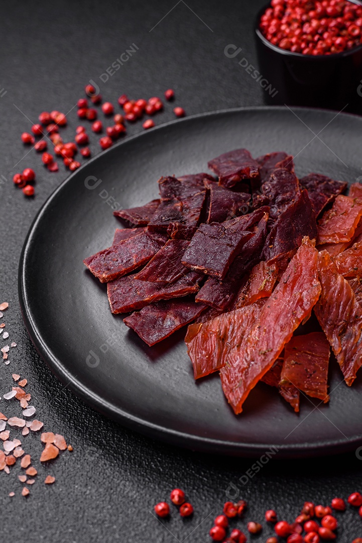 Deliciosa vitela seca ou carne seca de peru com sal, especiarias e ervas sobre um fundo escuro de concreto