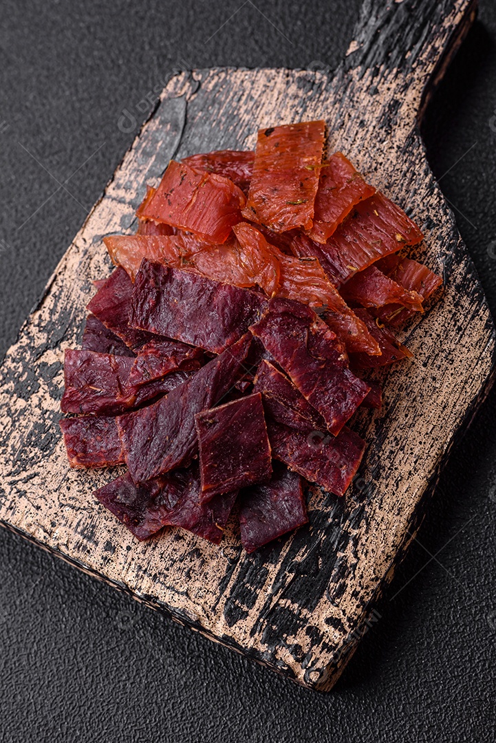 Deliciosa vitela seca ou carne seca de peru com sal, especiarias e ervas sobre um fundo escuro de concreto