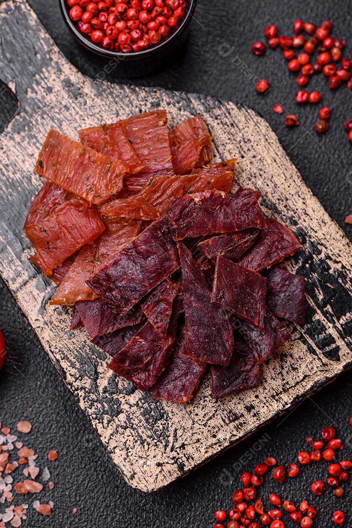 Deliciosa vitela seca ou carne seca de peru com sal, especiarias e ervas sobre um fundo escuro de concreto