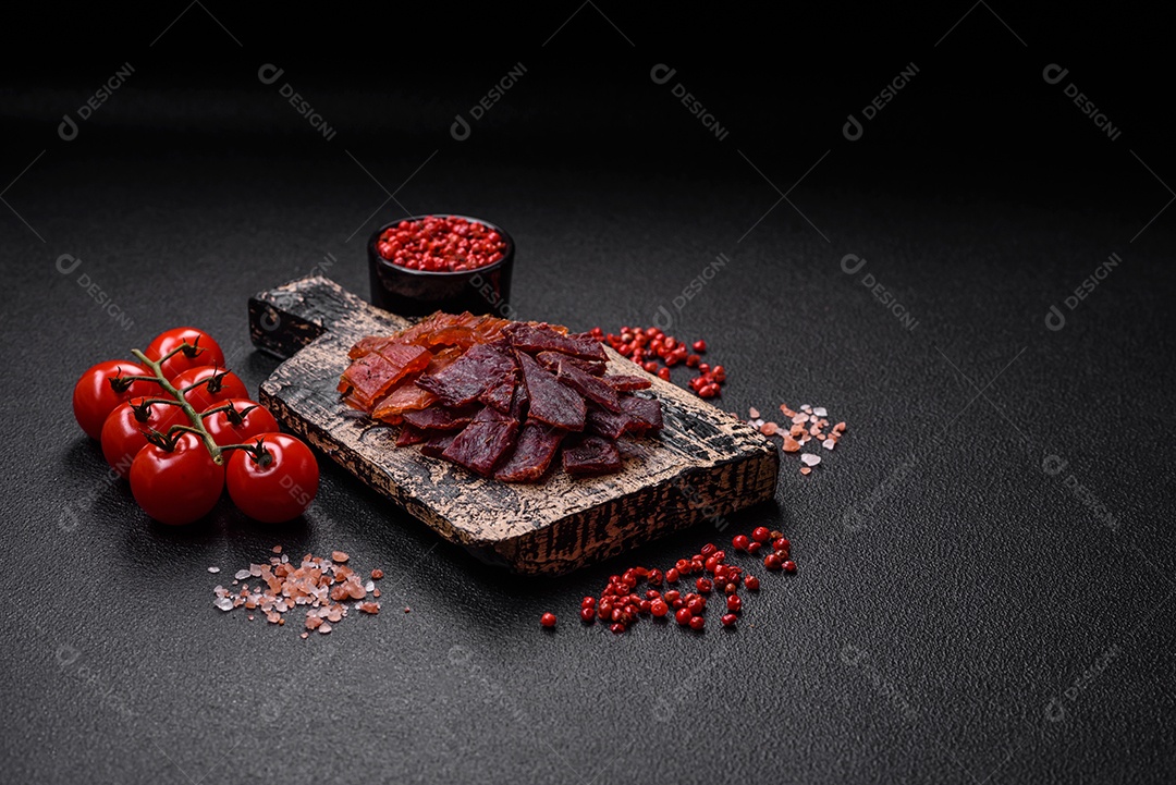 Deliciosa vitela seca ou carne seca de peru com sal, especiarias e ervas sobre um fundo escuro de concreto