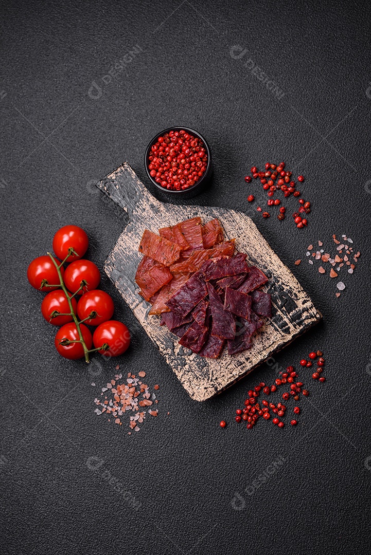 Deliciosa vitela seca ou carne seca de peru com sal, especiarias e ervas sobre um fundo escuro de concreto