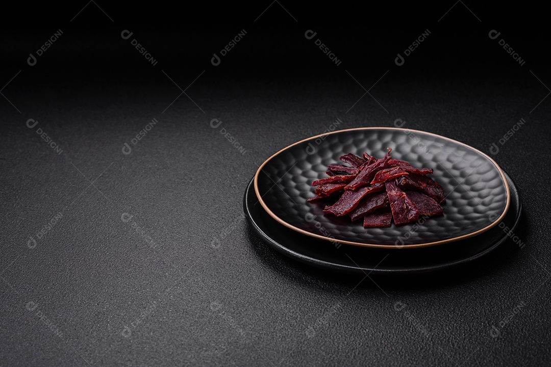 Deliciosa vitela seca ou carne seca de peru com sal, especiarias e ervas sobre um fundo escuro de concreto