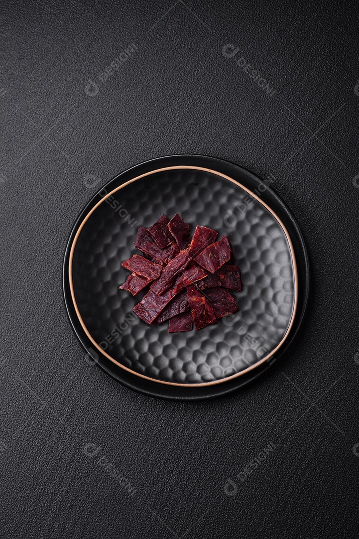 Deliciosa vitela seca ou carne seca de peru com sal, especiarias e ervas sobre um fundo escuro de concreto