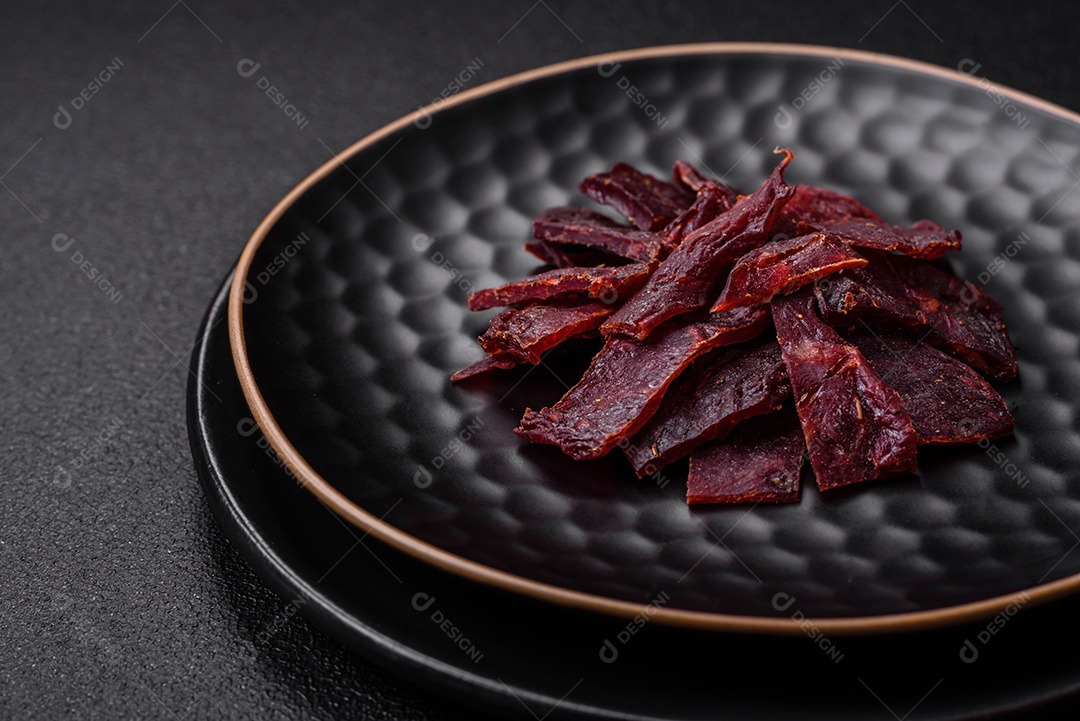 Deliciosa vitela seca ou carne seca de peru com sal, especiarias e ervas sobre um fundo escuro de concreto