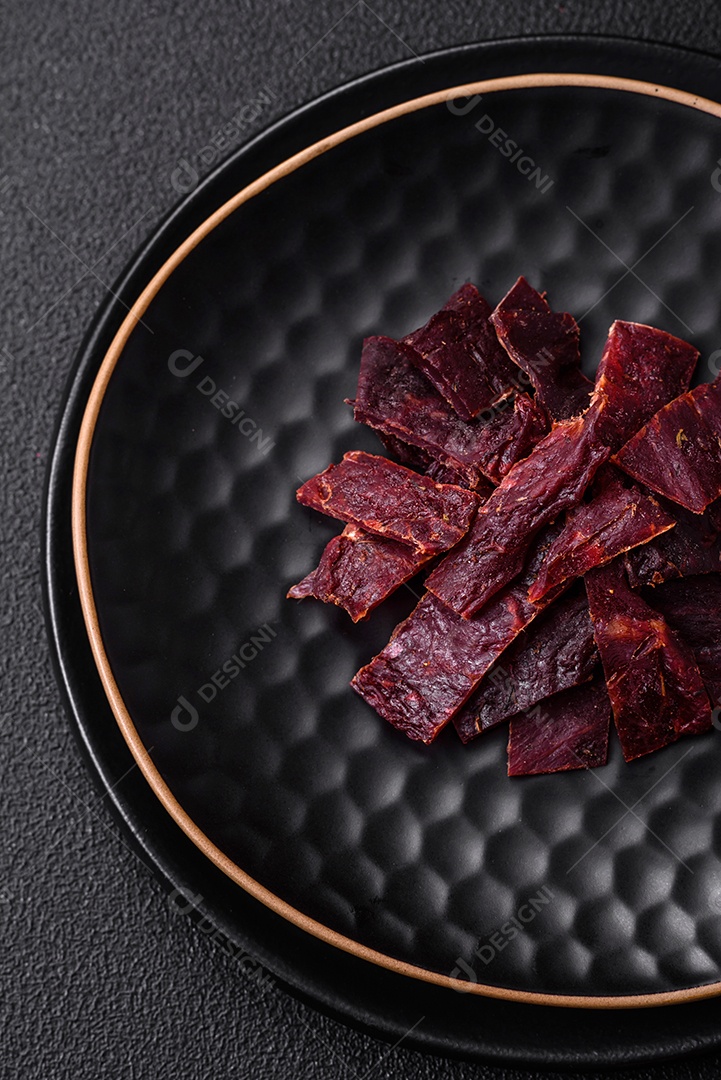 Deliciosa vitela seca ou carne seca de peru com sal, especiarias e ervas sobre um fundo escuro de concreto