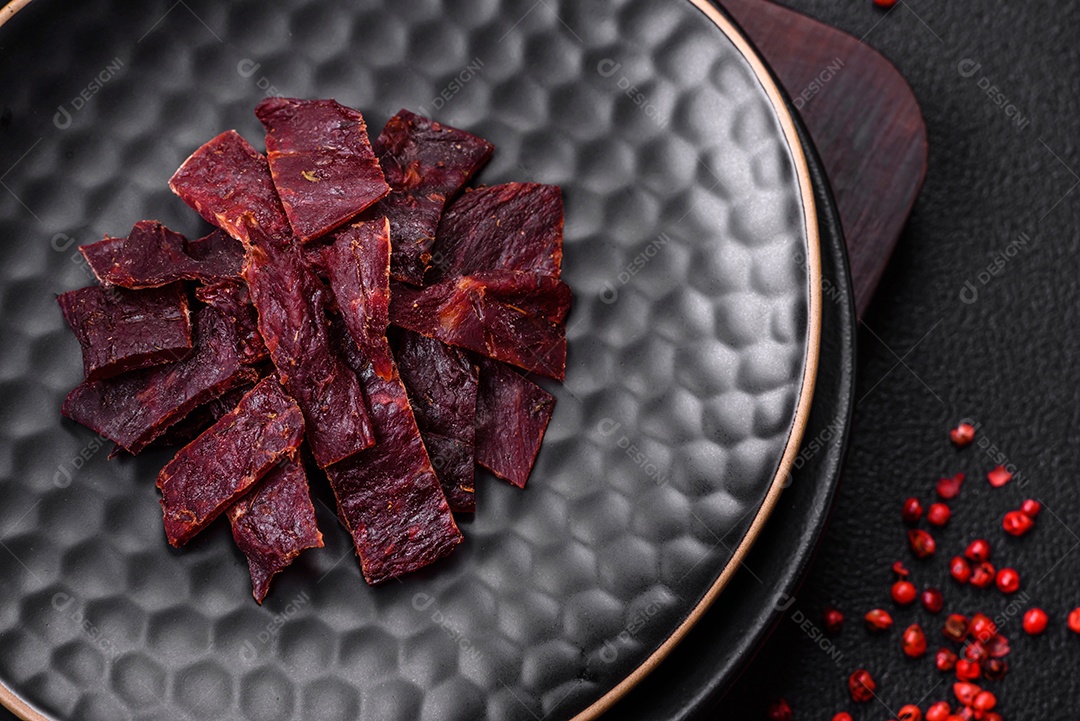 Deliciosa vitela seca ou carne seca de peru com sal, especiarias e ervas sobre um fundo escuro de concreto