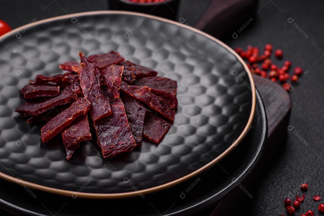 Deliciosa vitela seca ou carne seca de peru com sal, especiarias e ervas sobre um fundo escuro de concreto