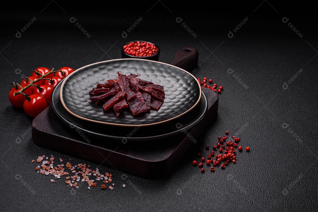 Deliciosa vitela seca ou carne seca de peru com sal, especiarias e ervas sobre um fundo escuro de concreto