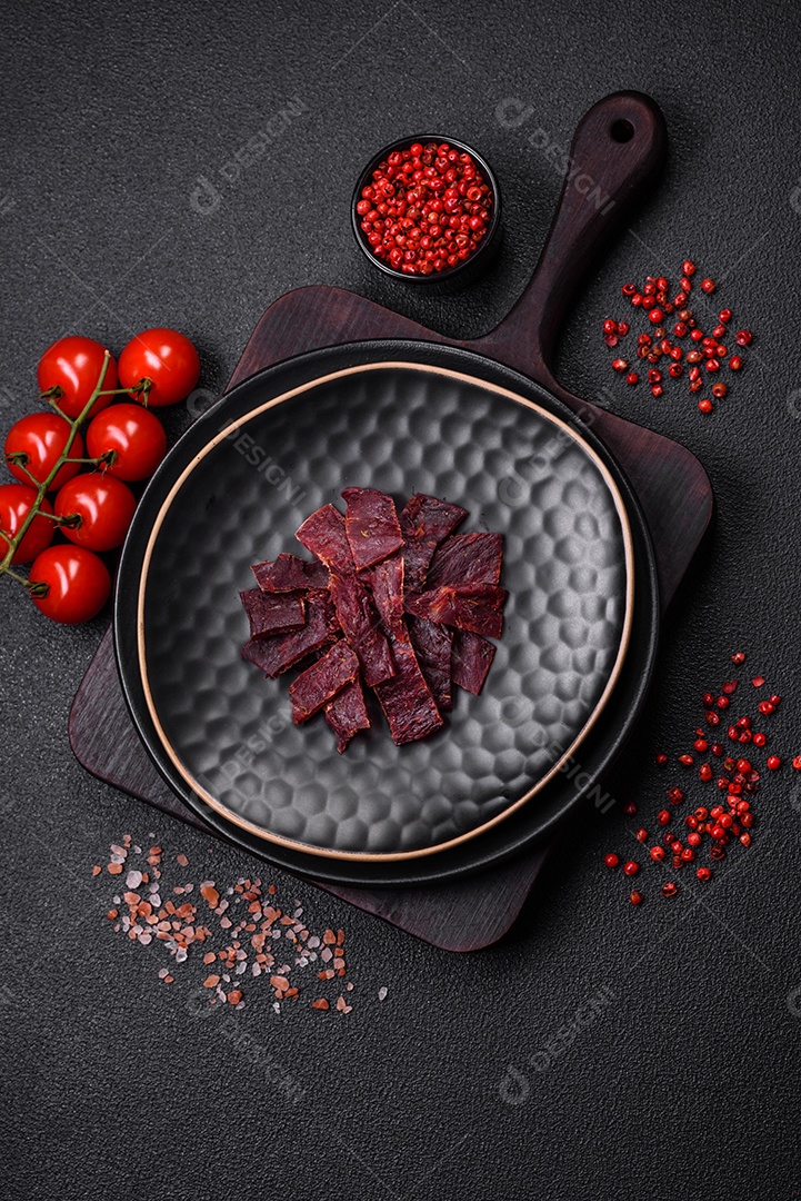 Deliciosa vitela seca ou carne seca de peru com sal, especiarias e ervas sobre um fundo escuro de concreto