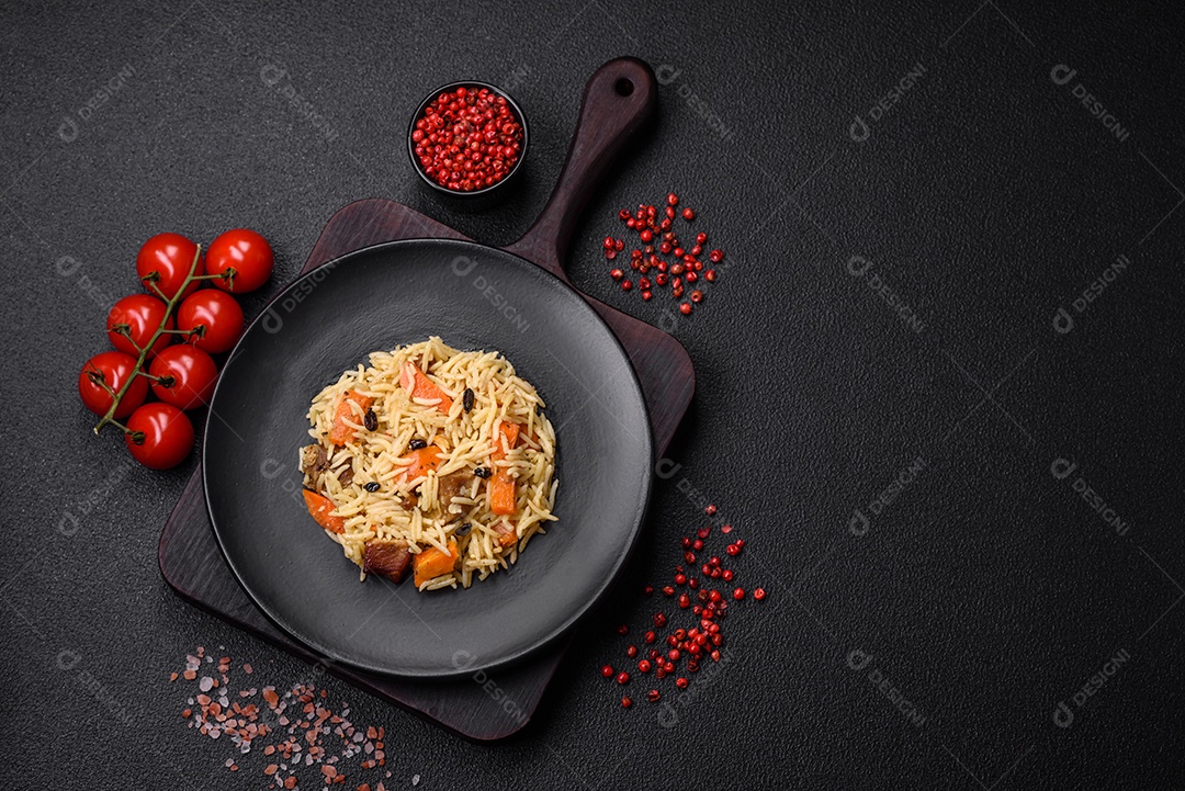 Delicioso pilaf uzbeque com frango, cenoura, bérberis, especiarias e ervas sobre um fundo escuro de concreto