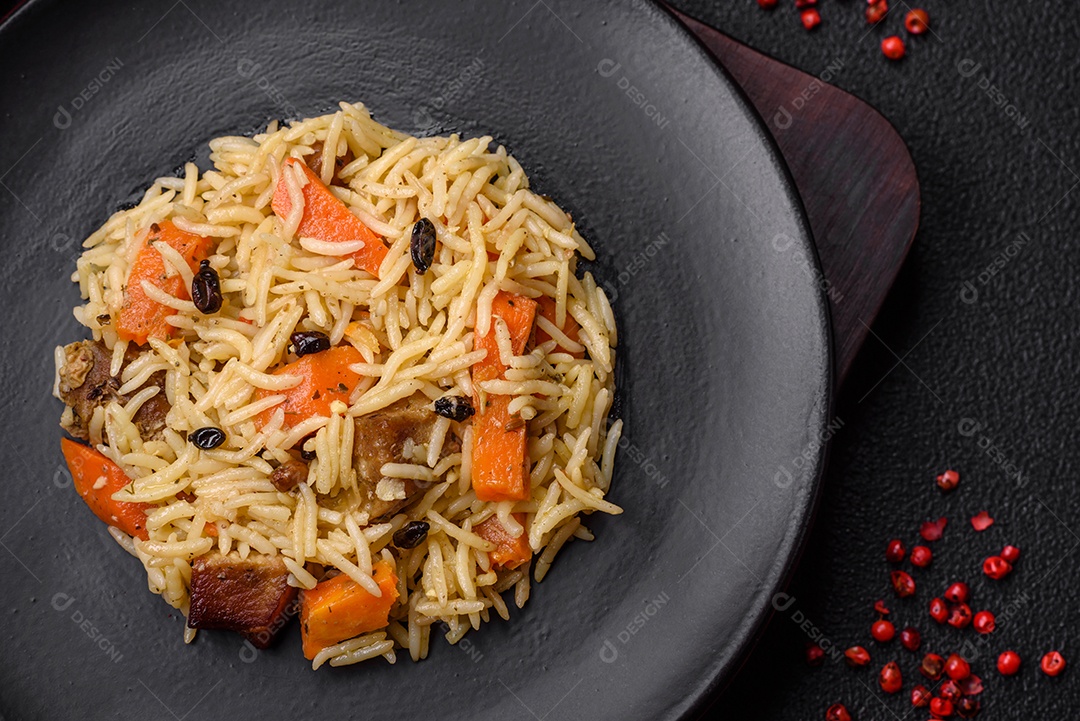 Delicioso pilaf uzbeque com frango, cenoura, bérberis, especiarias e ervas sobre um fundo escuro de concreto