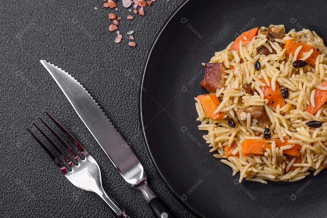 Delicioso pilaf uzbeque com frango, cenoura, bérberis, especiarias e ervas sobre um fundo escuro de concreto
