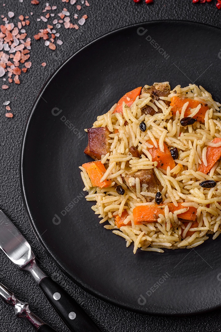 Delicioso pilaf uzbeque com frango, cenoura, bérberis, especiarias e ervas sobre um fundo escuro de concreto