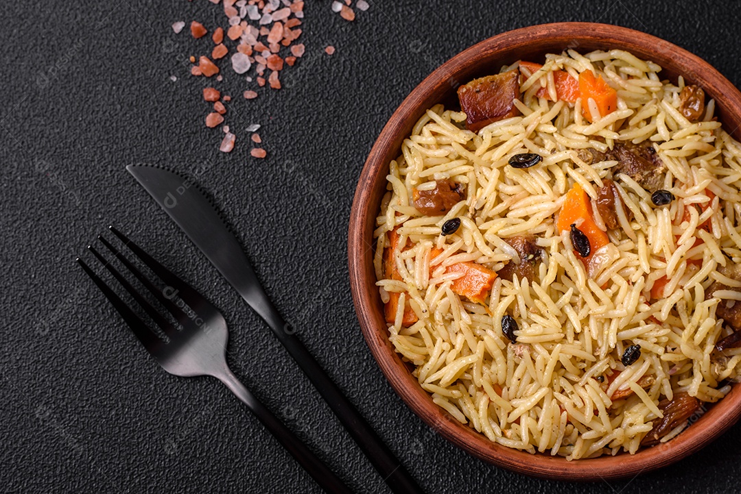 Delicioso pilaf uzbeque com frango, cenoura, bérberis, especiarias e ervas sobre um fundo escuro de concreto