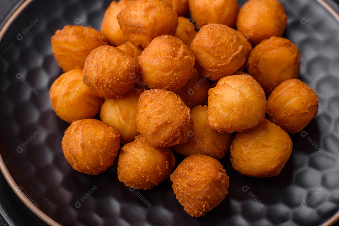 Deliciosas bolas de batata frita com mussarela à milanesa, sal, especiarias e ervas sobre um fundo escuro de concreto