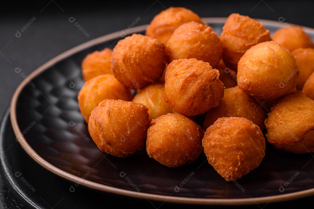 Deliciosas bolas de batata frita com mussarela à milanesa, sal, especiarias e ervas sobre um fundo escuro de concreto