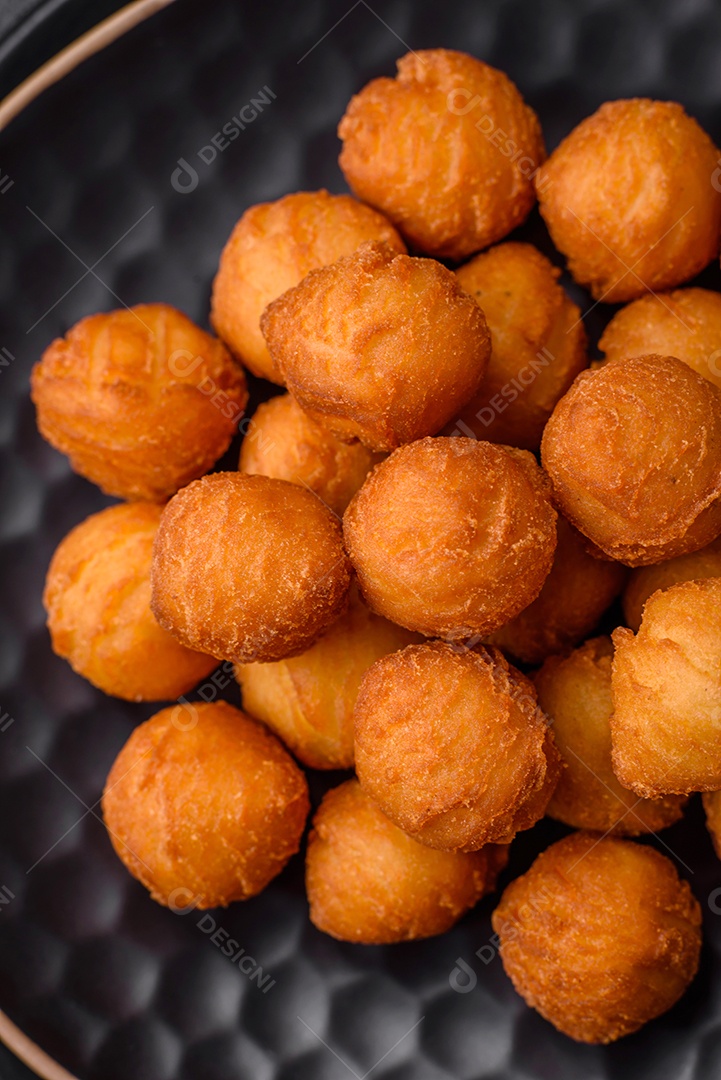 Deliciosas bolas de batata frita com mussarela à milanesa, sal, especiarias e ervas sobre um fundo escuro de concreto