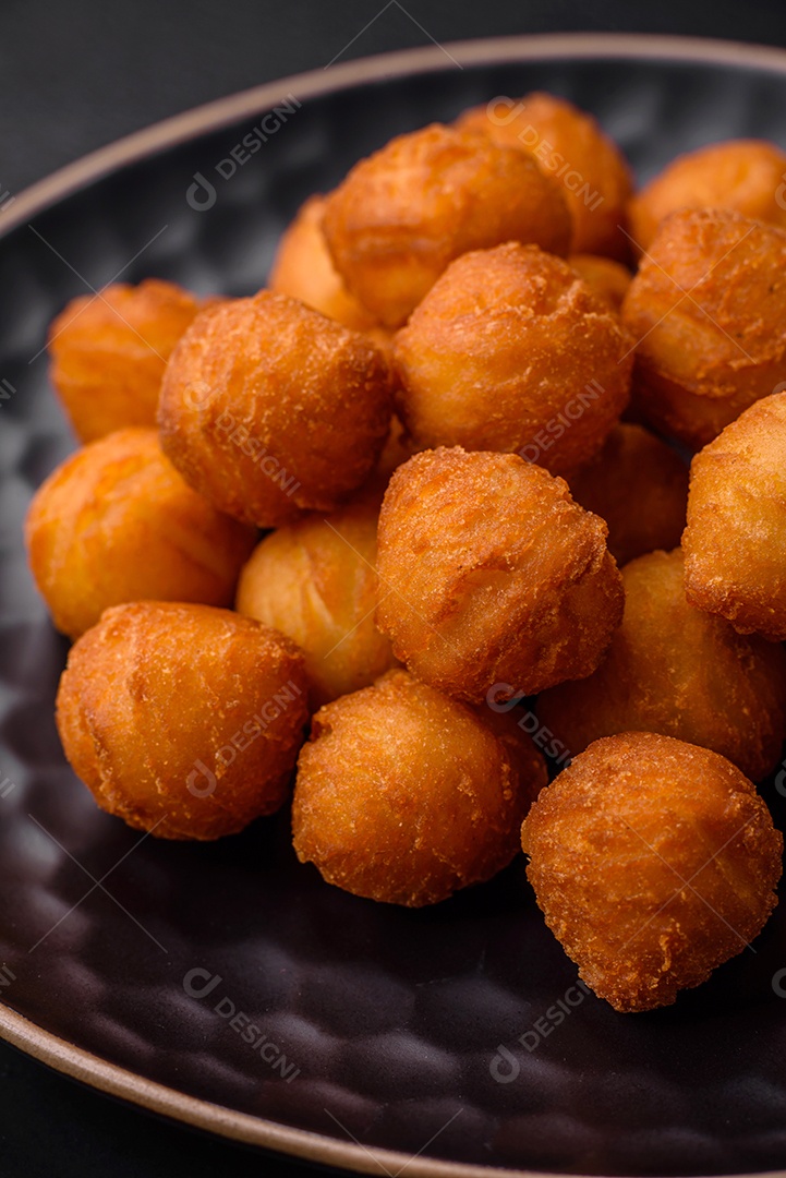 Deliciosas bolas de batata frita com mussarela à milanesa, sal, especiarias e ervas sobre um fundo escuro de concreto