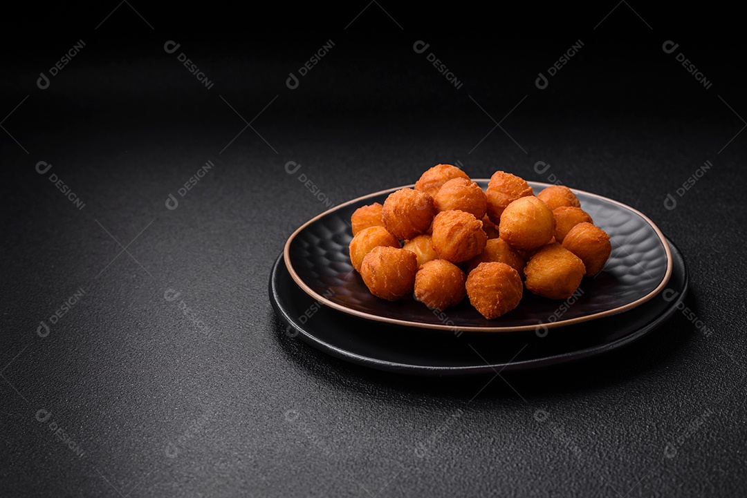 Deliciosas bolas de batata frita com mussarela à milanesa, sal, especiarias e ervas sobre um fundo escuro de concreto