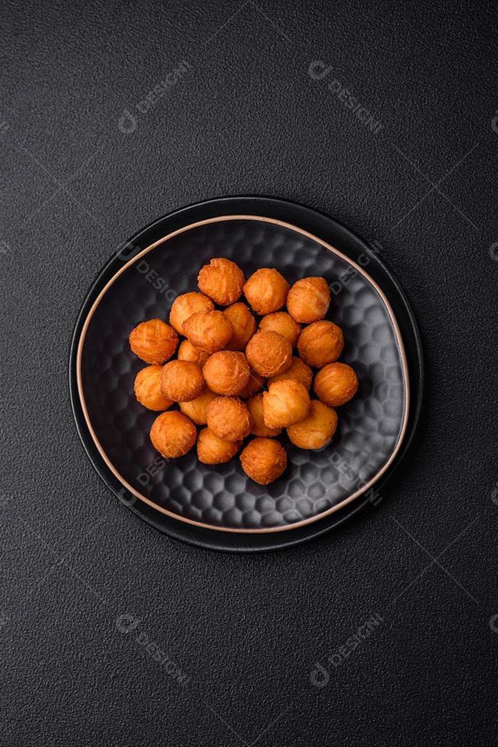 Deliciosas bolas de batata frita com mussarela à milanesa, sal, especiarias e ervas sobre um fundo escuro de concreto