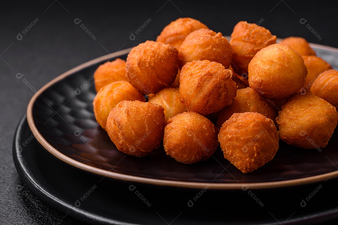 Deliciosas bolas de batata frita com mussarela à milanesa, sal, especiarias e ervas sobre um fundo escuro de concreto