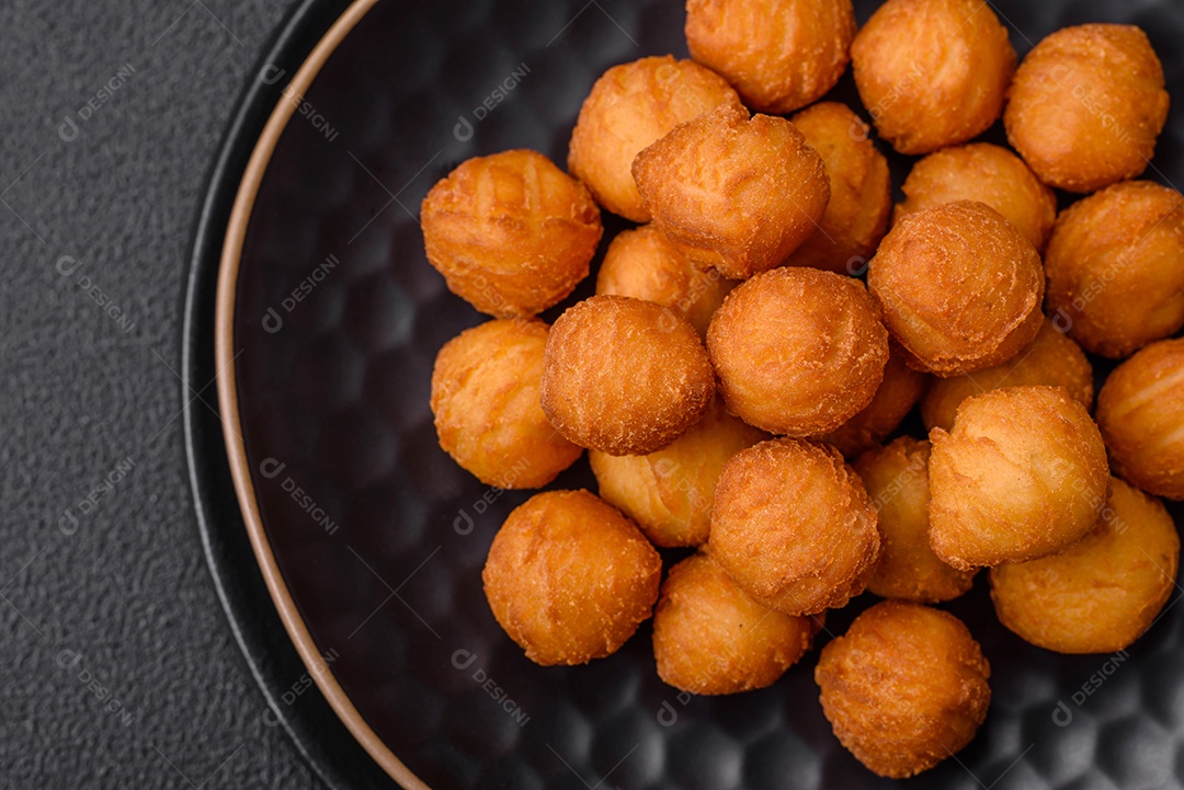 Deliciosas bolas de batata frita com mussarela à milanesa, sal, especiarias e ervas sobre um fundo escuro de concreto
