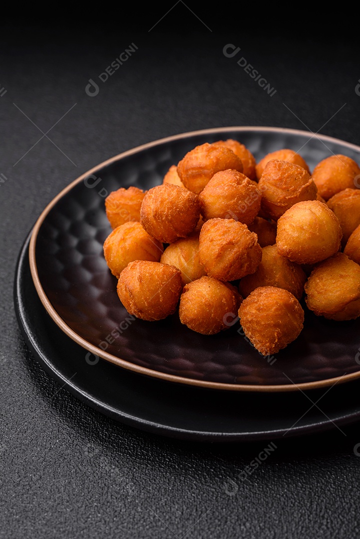 Deliciosas bolas de batata frita com mussarela à milanesa, sal, especiarias e ervas sobre um fundo escuro de concreto