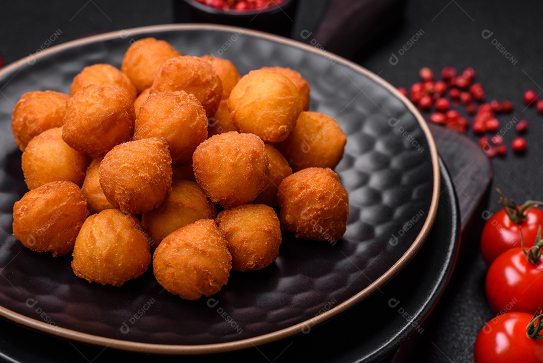 Deliciosas bolas de batata frita com mussarela à milanesa, sal, especiarias e ervas sobre um fundo escuro de concreto