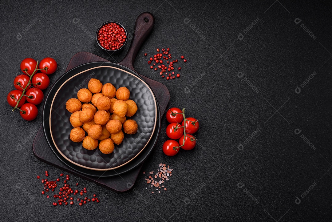 Deliciosas bolas de batata frita com mussarela à milanesa, sal, especiarias e ervas sobre um fundo escuro de concreto