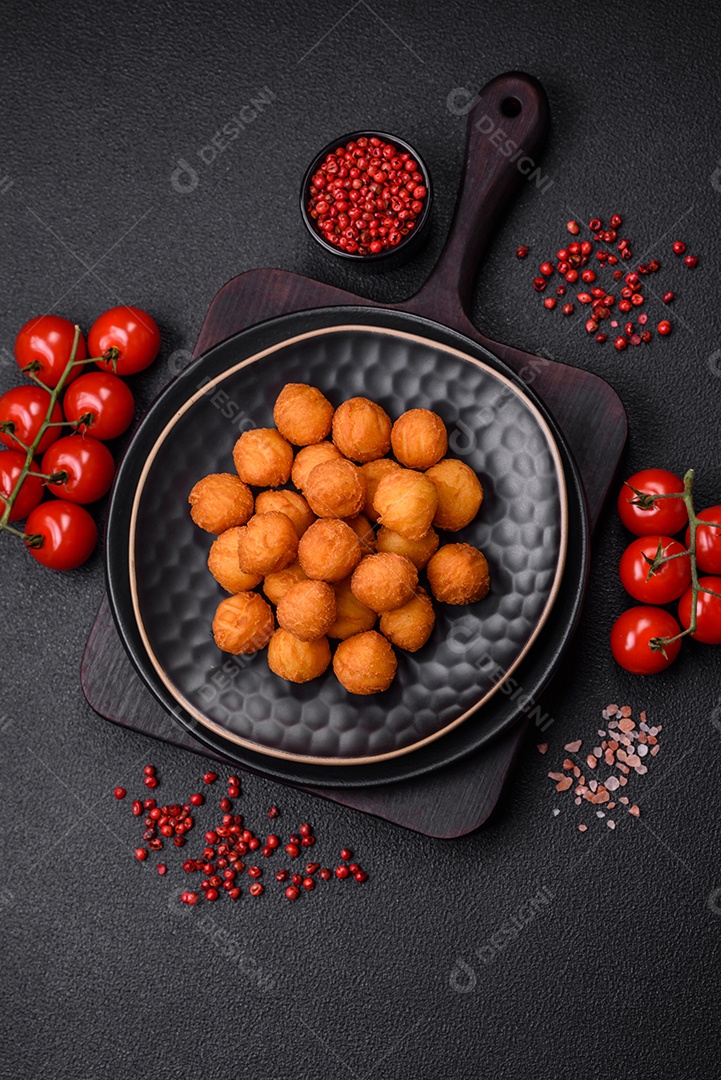 Deliciosas bolas de batata frita com mussarela à milanesa, sal, especiarias e ervas sobre um fundo escuro de concreto