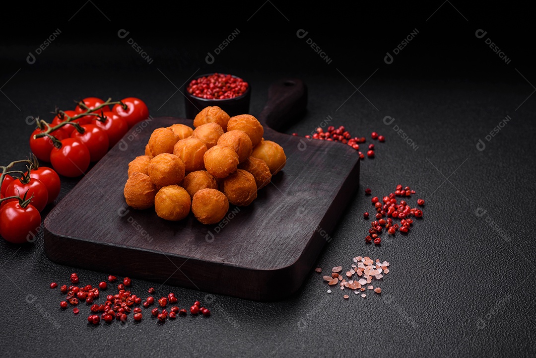 Deliciosas bolas de batata frita com mussarela à milanesa, sal, especiarias e ervas sobre um fundo escuro de concreto