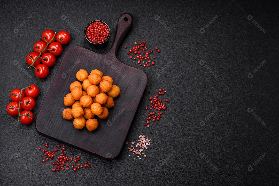 Deliciosas bolas de batata frita com mussarela à milanesa, sal, especiarias e ervas sobre um fundo escuro de concreto