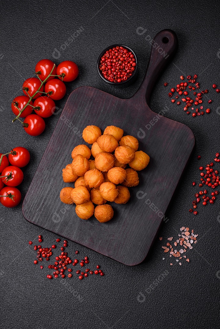Deliciosas bolas de batata frita com mussarela à milanesa, sal, especiarias e ervas sobre um fundo escuro de concreto