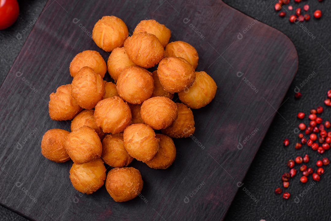 Deliciosas bolas de batata frita com mussarela à milanesa, sal, especiarias e ervas sobre um fundo escuro de concreto