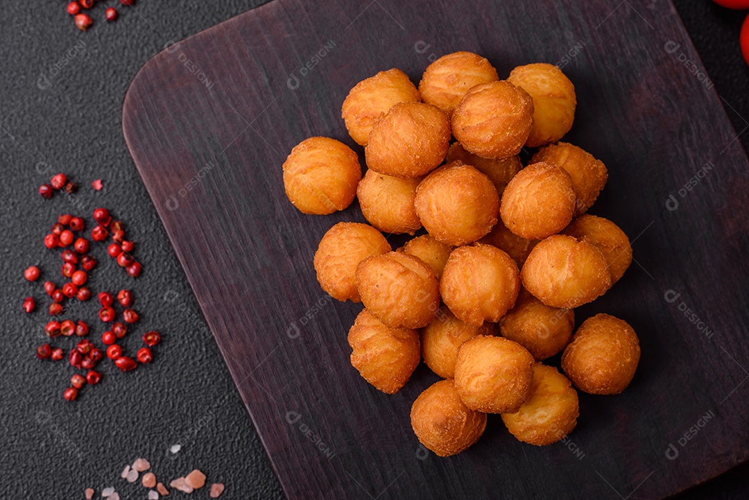 Deliciosas bolas de batata frita com mussarela à milanesa, sal, especiarias e ervas sobre um fundo escuro de concreto