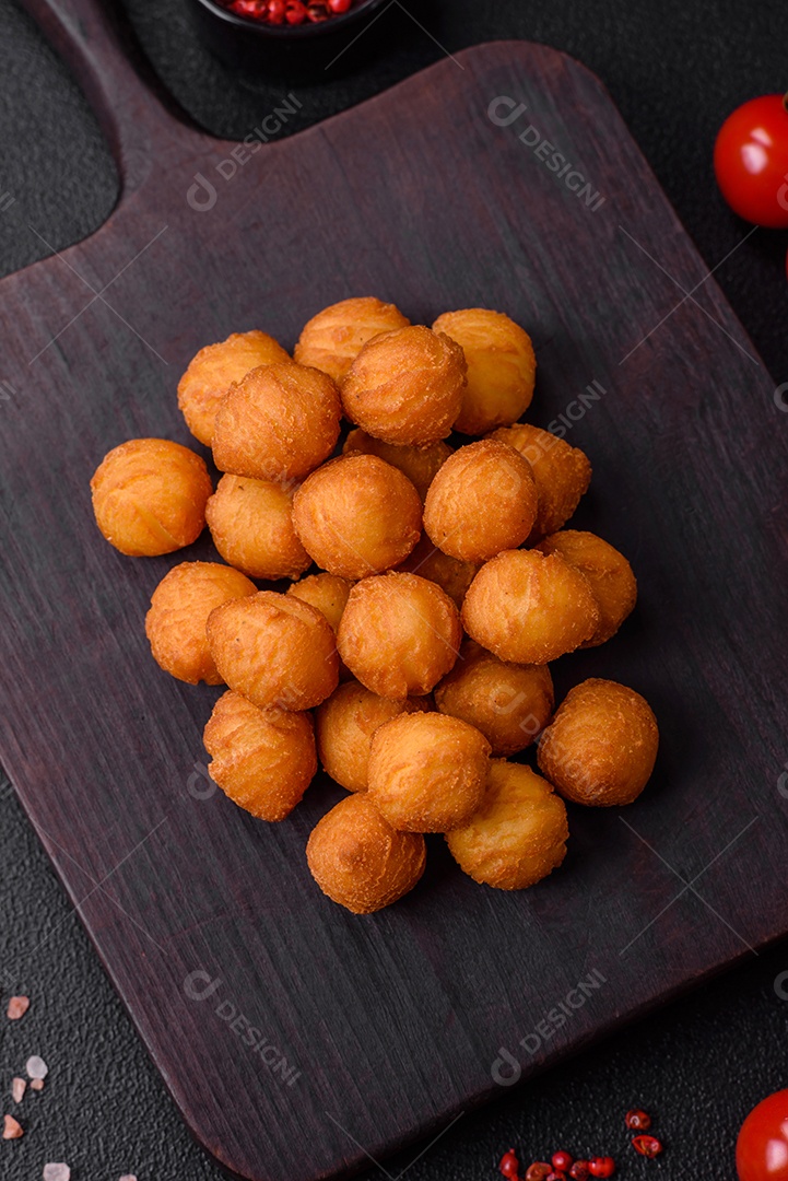 Deliciosas bolas de batata frita com mussarela à milanesa, sal, especiarias e ervas sobre um fundo escuro de concreto