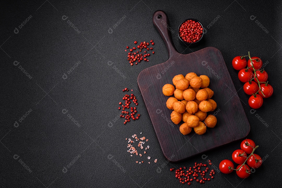 Deliciosas bolas de batata frita com mussarela à milanesa, sal, especiarias e ervas sobre um fundo escuro de concreto