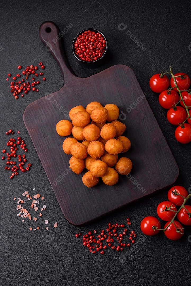 Deliciosas bolas de batata frita com mussarela à milanesa, sal, especiarias e ervas sobre um fundo escuro de concreto
