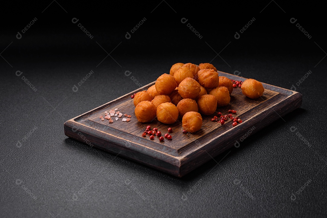 Deliciosas bolas de batata frita com mussarela à milanesa, sal, especiarias e ervas sobre um fundo escuro de concreto