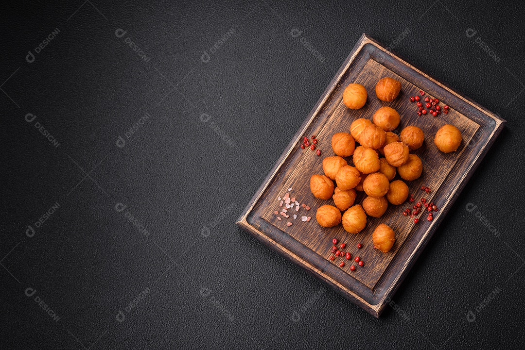 Deliciosas bolas de batata frita com mussarela à milanesa, sal, especiarias e ervas sobre um fundo escuro de concreto