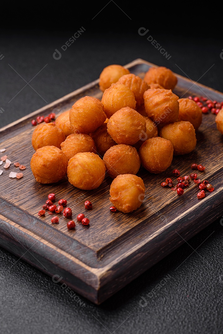 Deliciosas bolas de batata frita com mussarela à milanesa, sal, especiarias e ervas sobre um fundo escuro de concreto