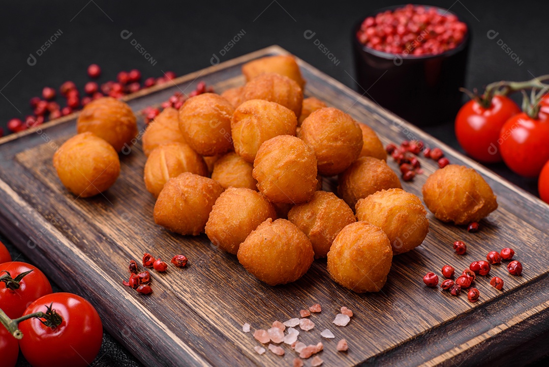 Deliciosas bolas de batata frita com mussarela à milanesa, sal, especiarias e ervas sobre um fundo escuro de concreto