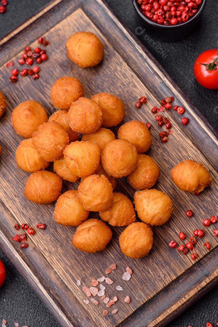 Deliciosas bolas de batata frita com mussarela à milanesa, sal, especiarias e ervas sobre um fundo escuro de concreto