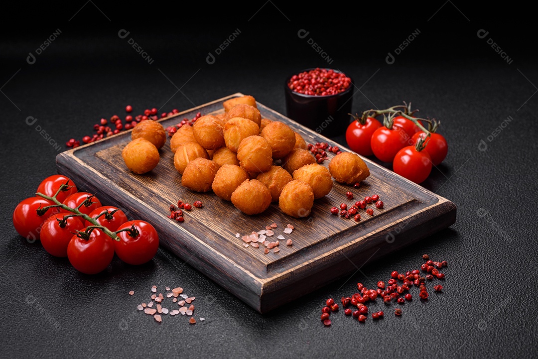 Deliciosas bolas de batata frita com mussarela à milanesa, sal, especiarias e ervas sobre um fundo escuro de concreto