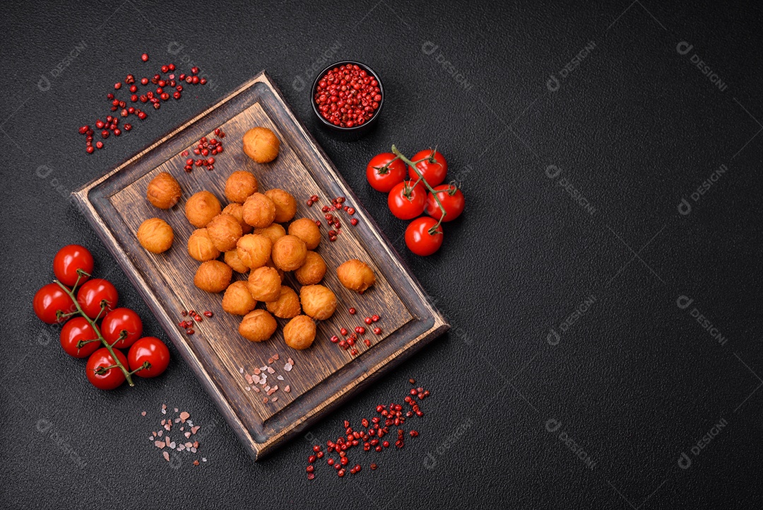 Deliciosas bolas de batata frita com mussarela à milanesa, sal, especiarias e ervas sobre um fundo escuro de concreto